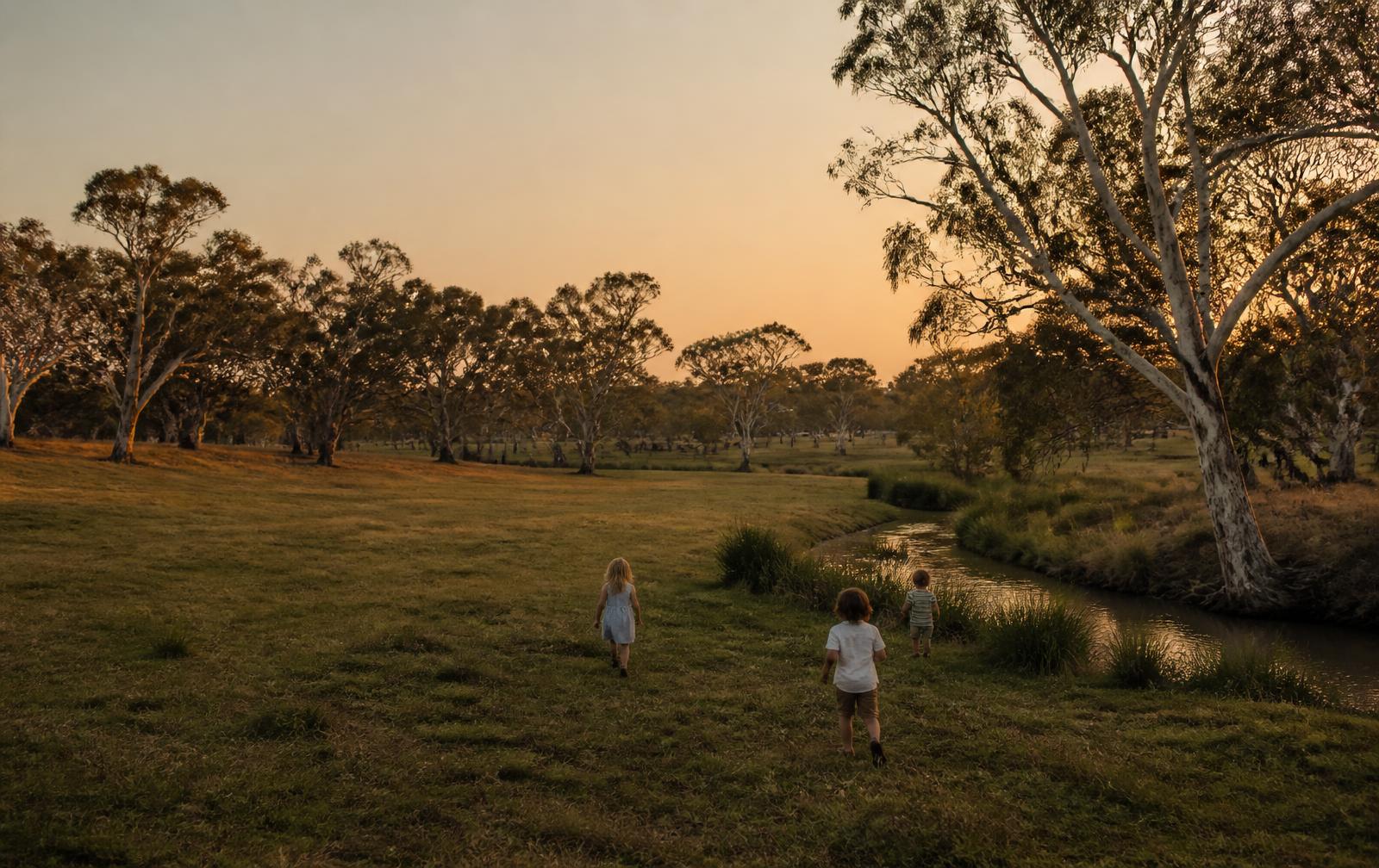 Children walking together across an open grassy park at sunset